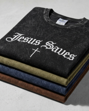 A vertical stack of four folded Colortone 1300 mineral wash t-shirts in Black, Olive, Navy, and Brown, showing the "Jesus Saves" embroidery on the top black shirt.
